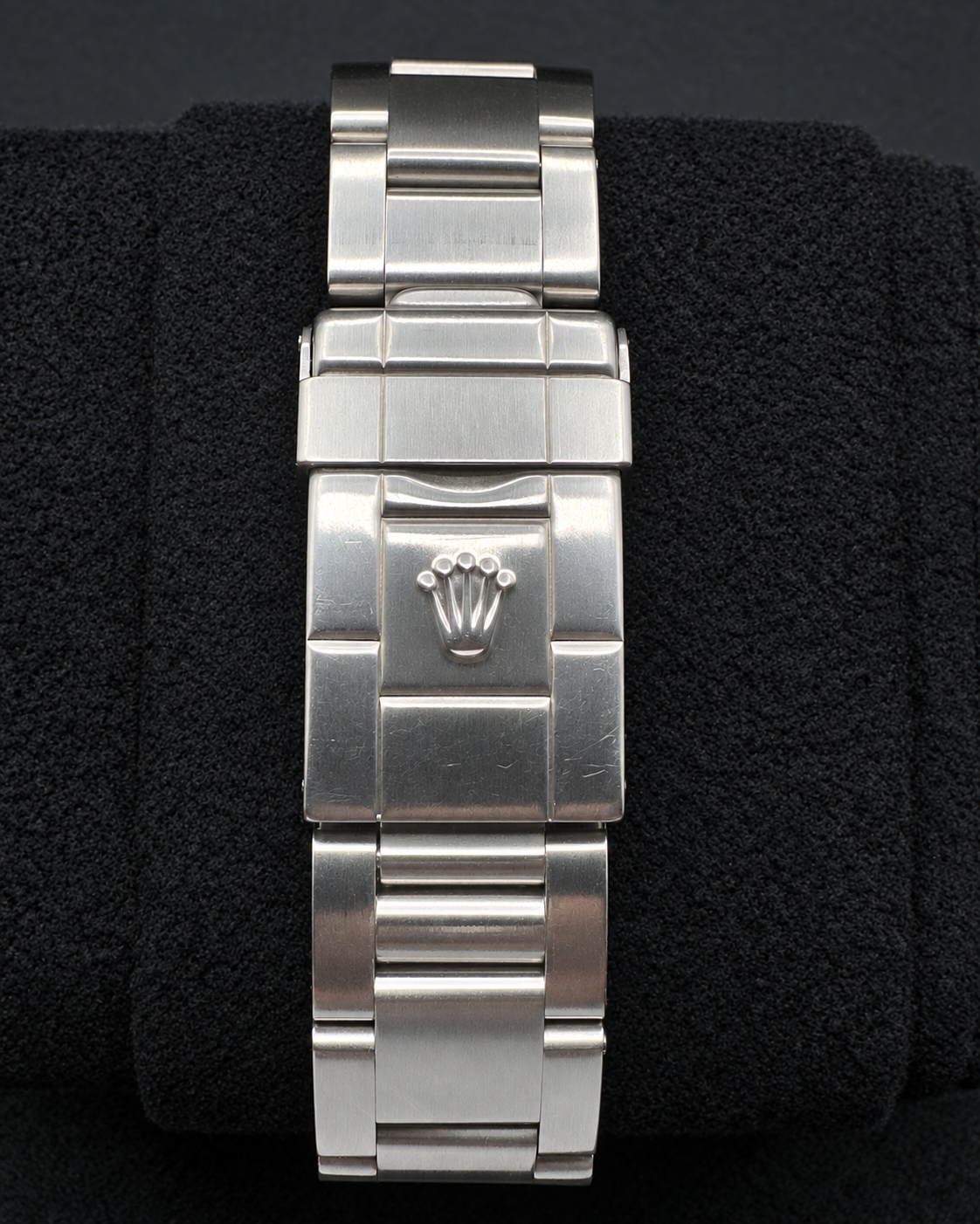 A silver stainless steel watch band with a central crown logo, displayed on a black textured background.