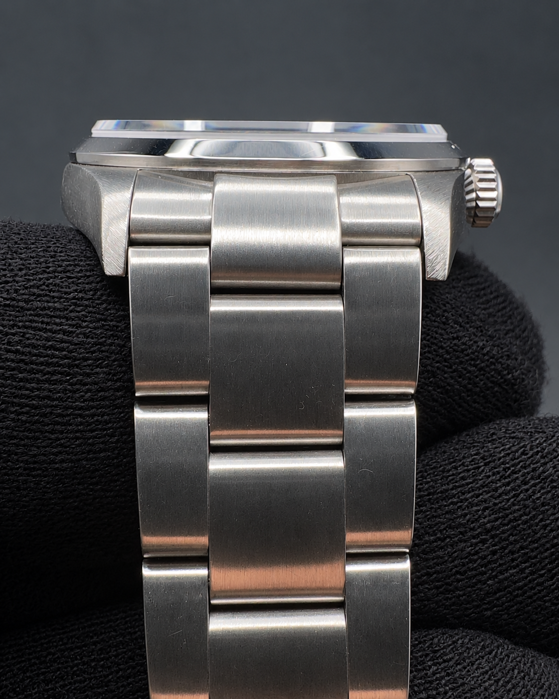 Close-up rear view of a stainless steel wristwatch with a metal link bracelet, shown resting on a black textured surface against a dark gray background.