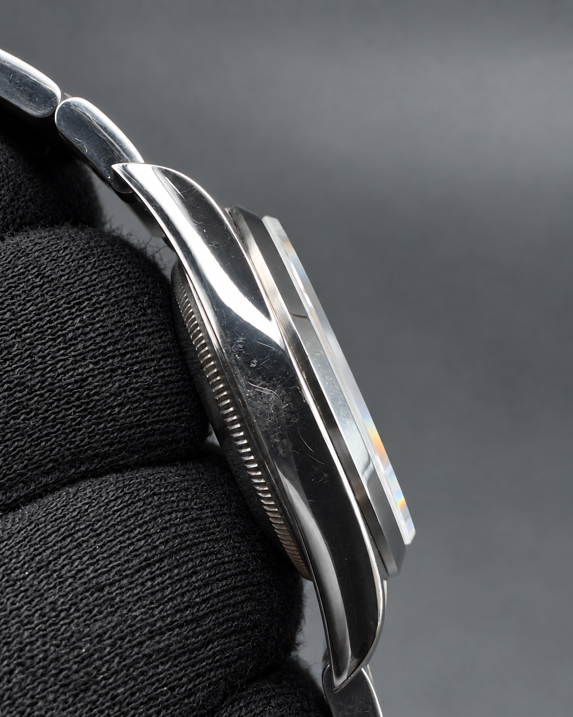 Close-up of a silver-toned metal watch case and bracelet held against a black textured fabric background.
