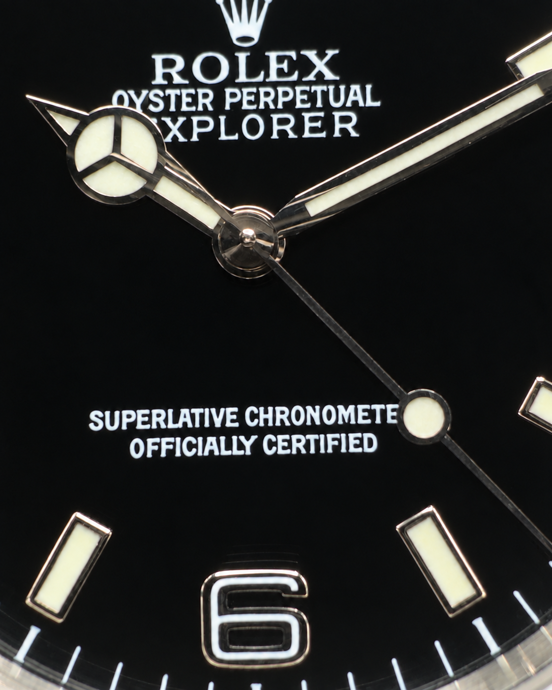Close-up of a Rolex Oyster Perpetual Explorer watch dial, showing the black face, white and silver hour markers and hands, and the Rolex crown logo at the top.