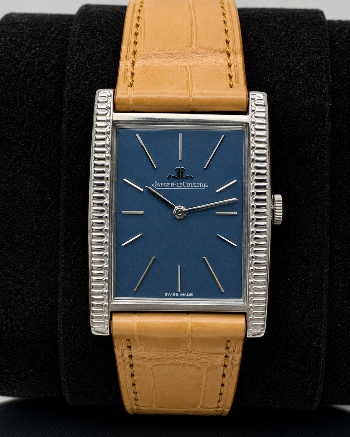 A vintage Jaeger-LeCoultre watch with a blue dial, silver-tone fluted case, and a tan leather strap, displayed on a black velvet cushion.