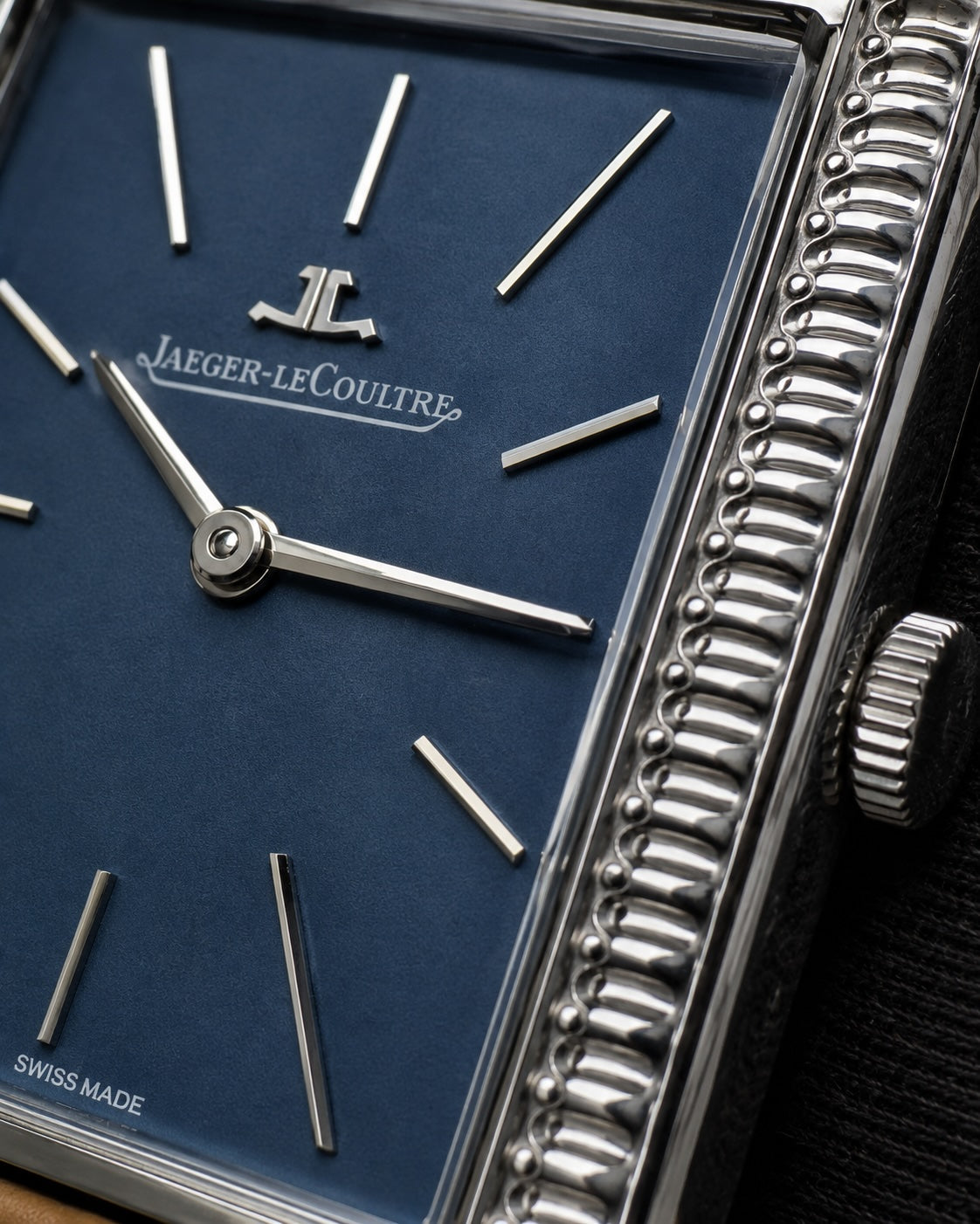 Close-up of a Jaeger-LeCoultre watch with a deep blue dial, silver-tone baton indices, and a highly polished beaded stainless steel case.