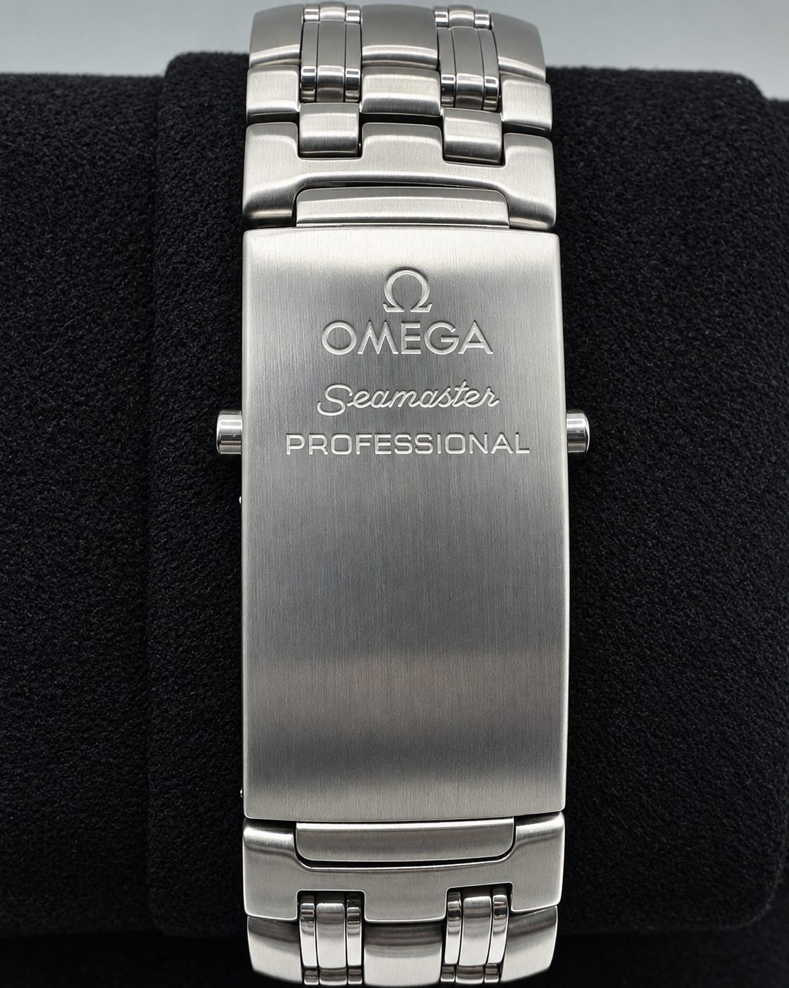 Omega Seamaster Professional stainless steel watch band clasp, featuring a brushed silver metal surface with engraved branding, displayed on a black textured velvet cushion.