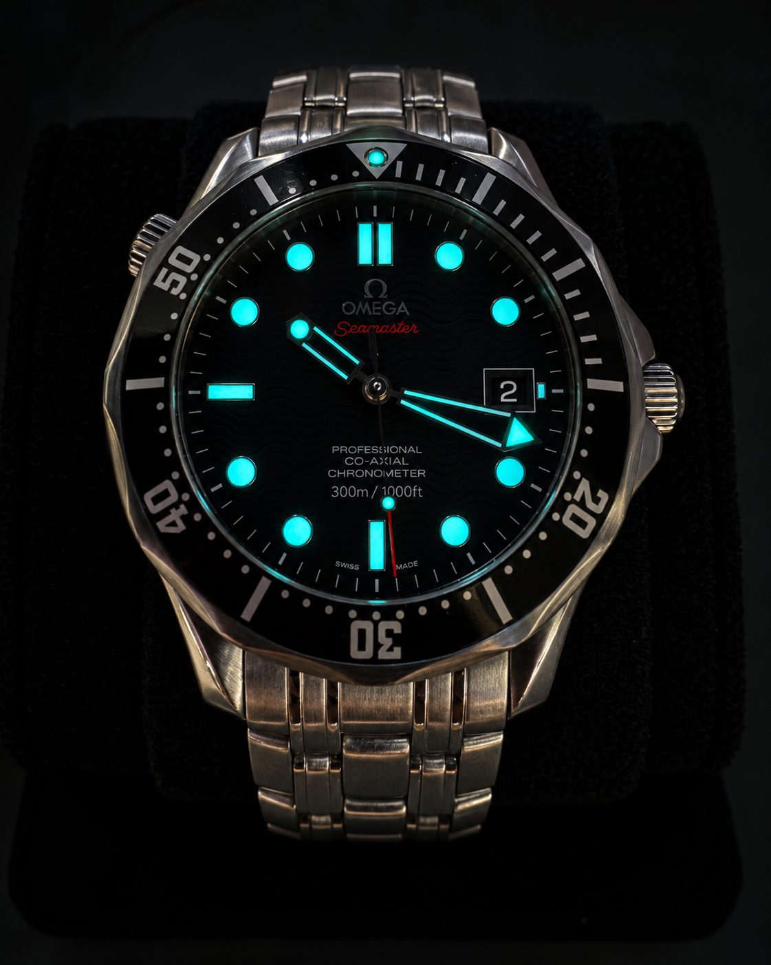 Omega Seamaster Professional diver watch with a black dial, luminous blue markers and hands, and a brushed stainless steel case and bracelet, displayed on a black velvet cushion.