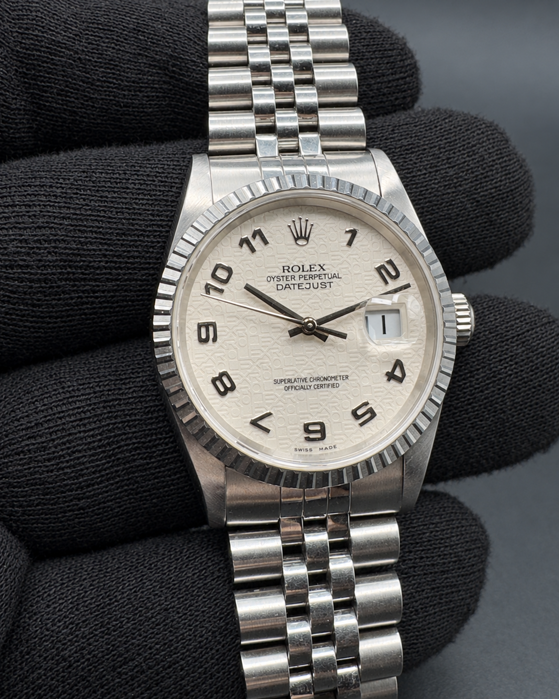 Rolex Datejust 16220 held in a gloved hand, showing the white patterned dial, bezel and Jubilee bracelet.