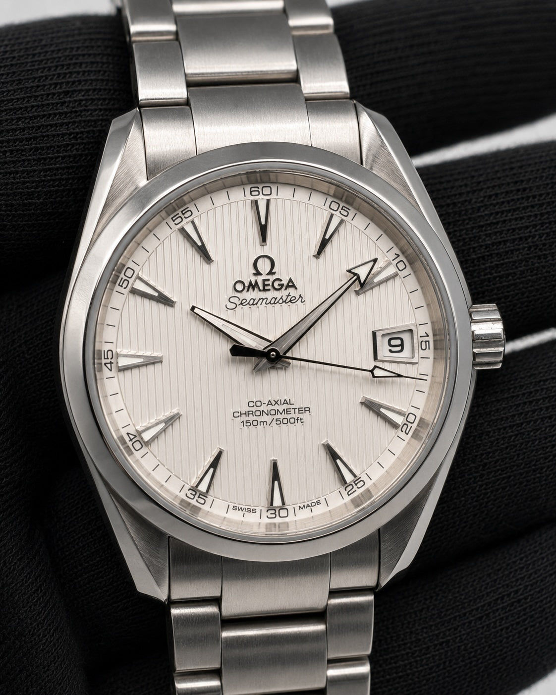 Omega Seamaster stainless steel watch with a silver dial and matching metal bracelet, shown close-up against a black textured background.