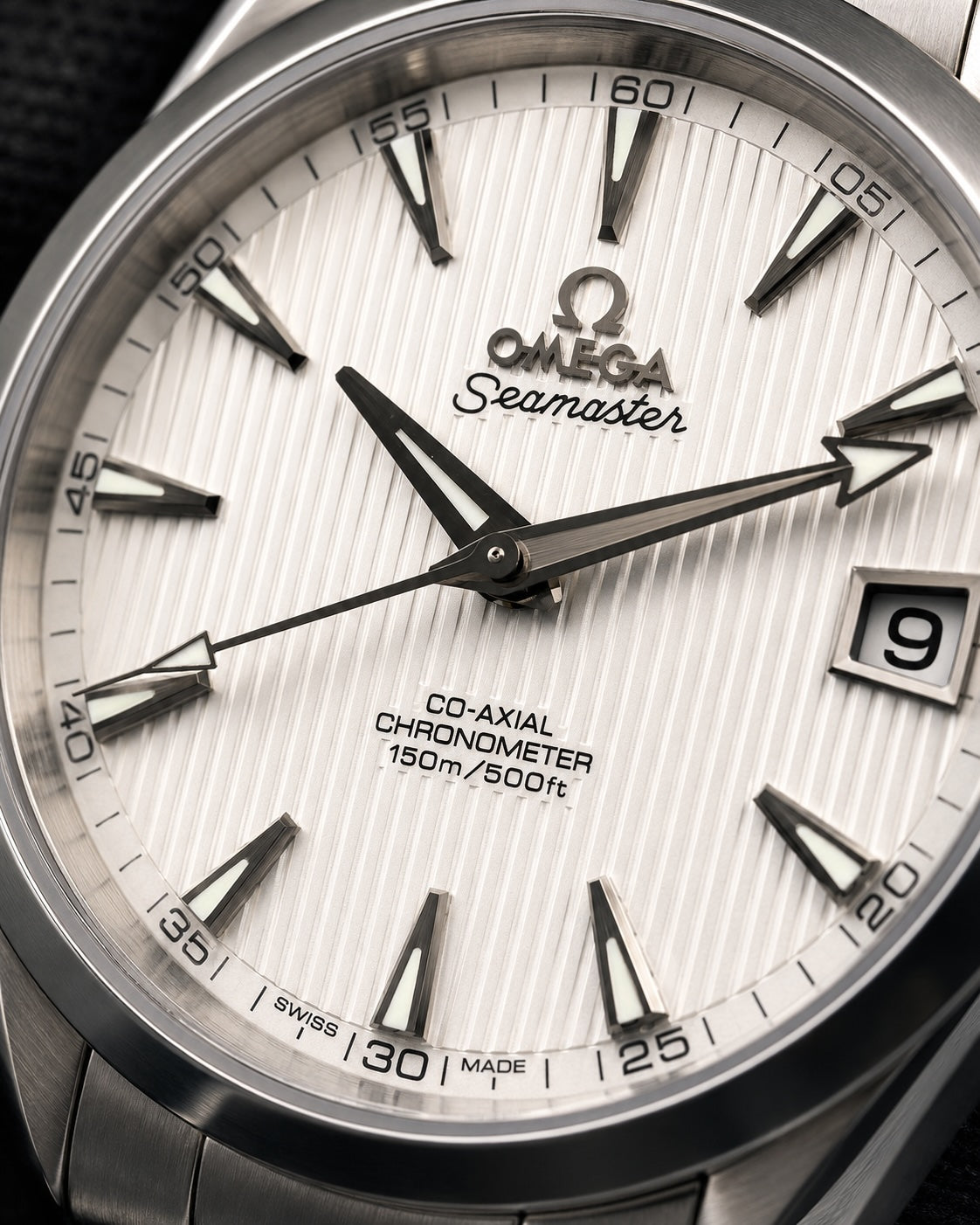 Close-up of an Omega Seamaster Co-Axial Chronometer watch dial, showing a silver sunburst textured face with black hands, baton indices, and a date window displaying the number 9.