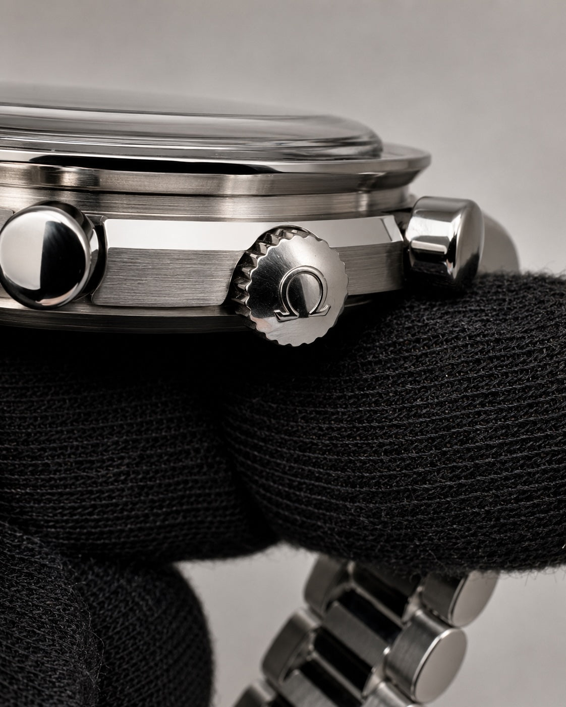 Close-up of a stainless steel wristwatch with a brushed and polished metal case, featuring a prominent crown knob with an Omega logo and a matching metal bracelet, shown resting on a black textured surface.