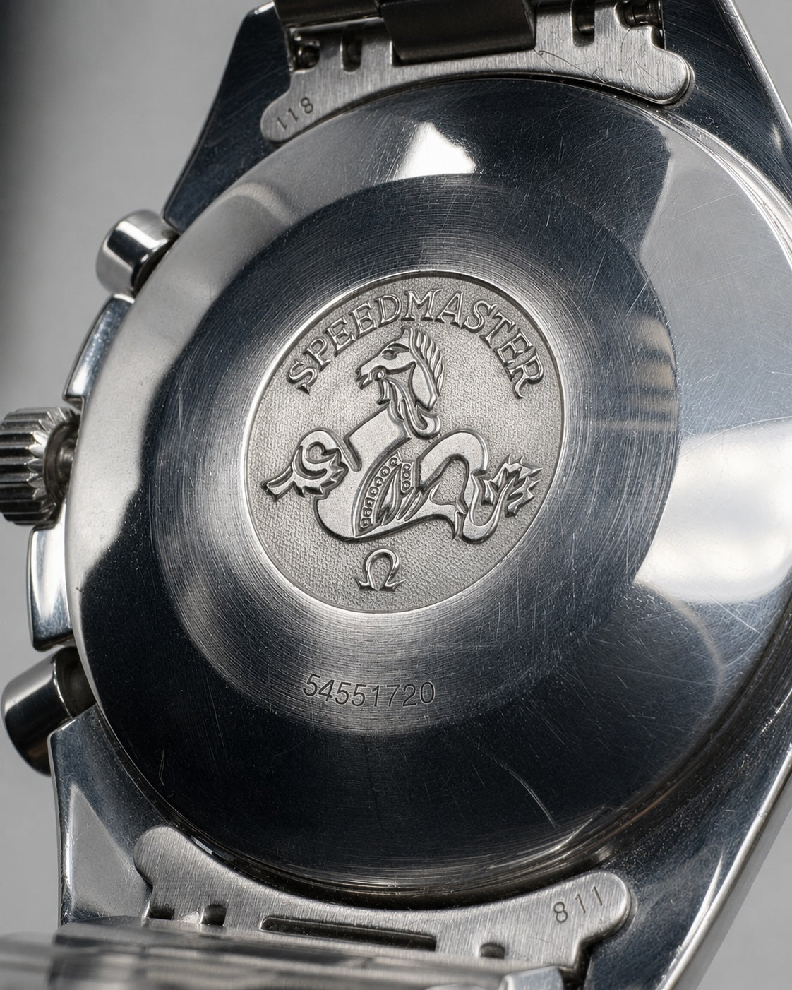 Close-up of the back of a stainless steel wristwatch showing the Speedmaster logo and crown details engraved on the polished case.