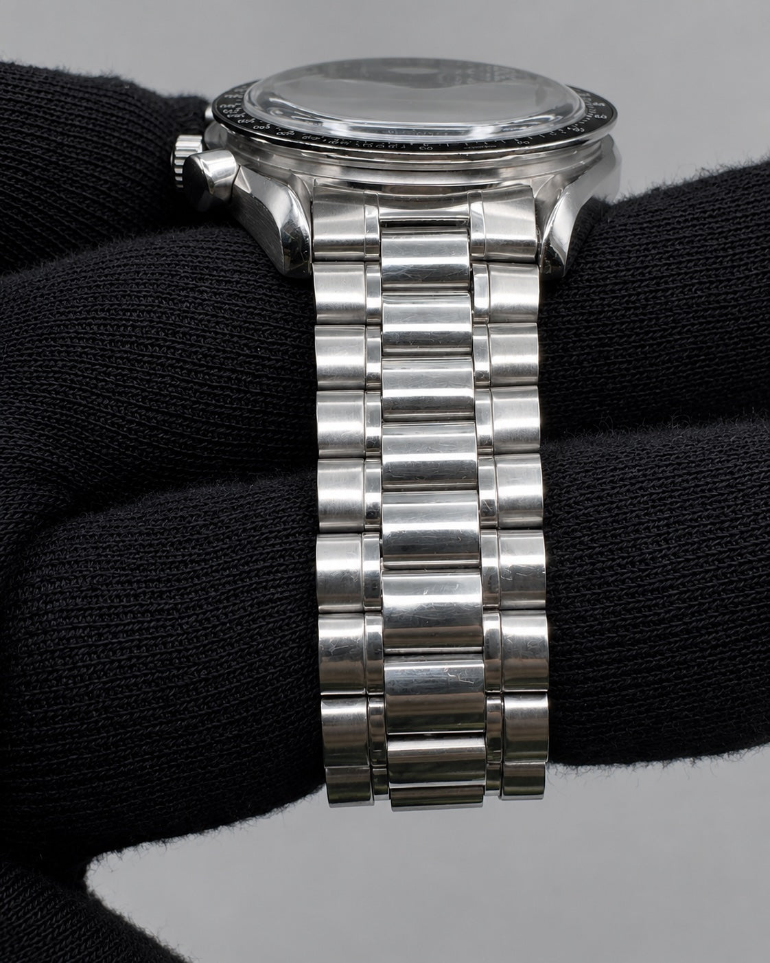A stainless steel watch with a multi-link bracelet, shown resting on a black knit glove against a neutral gray background.