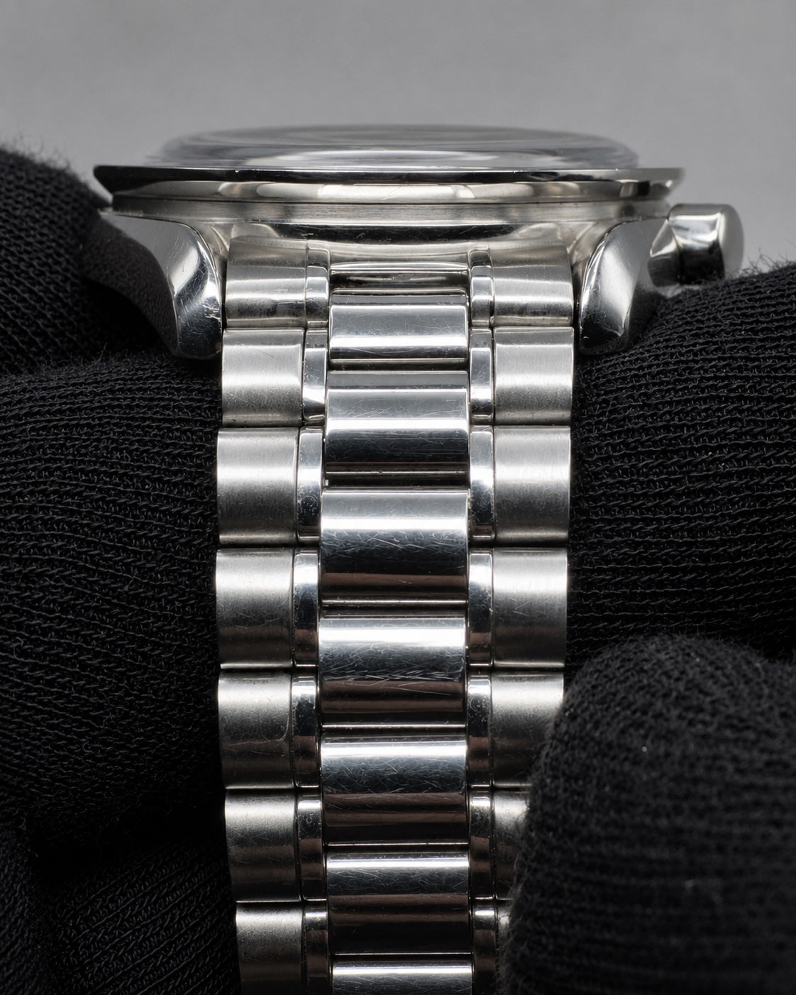 Close-up of a stainless steel watch band with a polished silver-tone metal link design, shown resting on a black textured fabric surface.