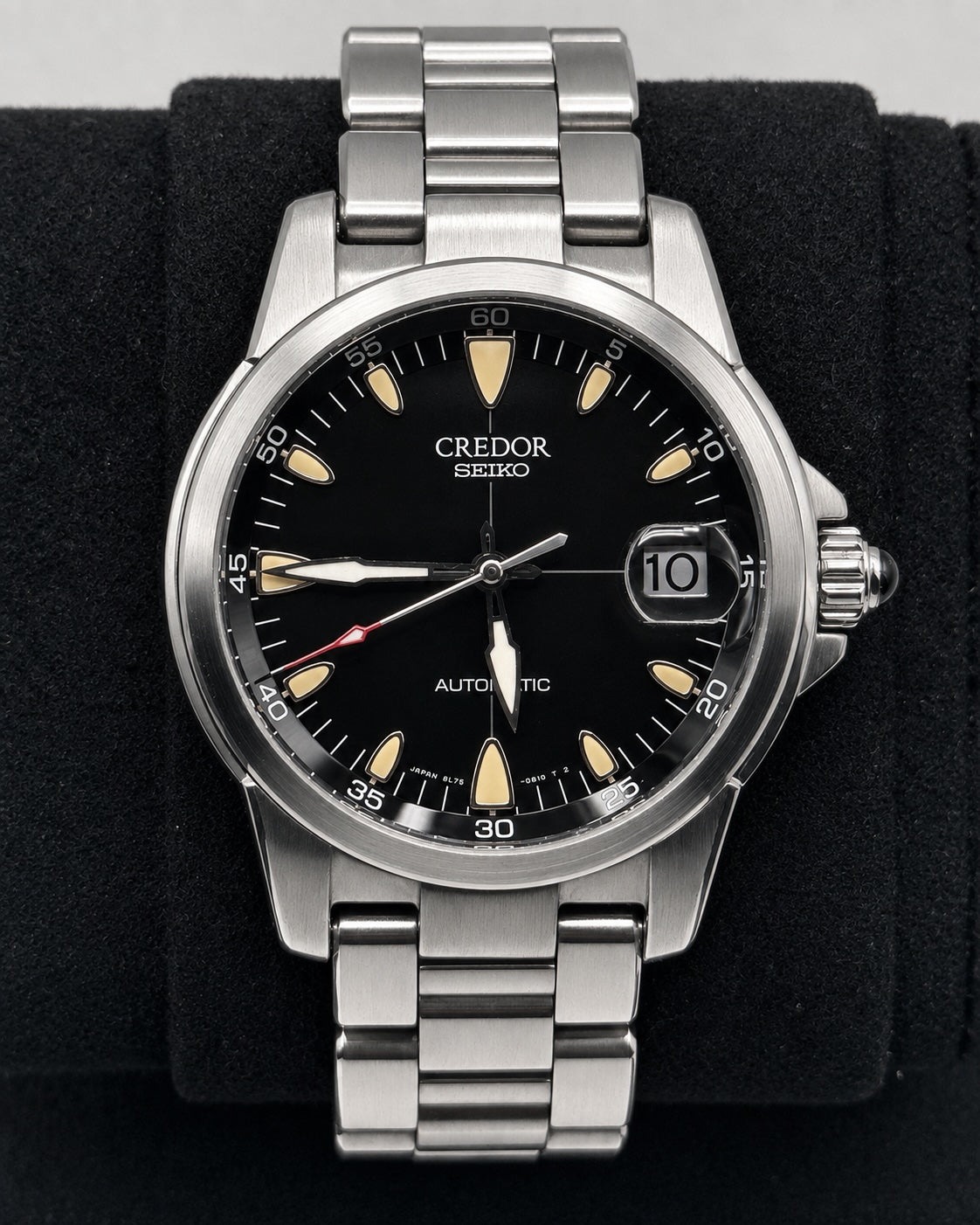 A stainless steel Credor Seiko automatic watch with a black dial, cream-colored hour markers, and a date window, displayed on a black velvet watch cushion.