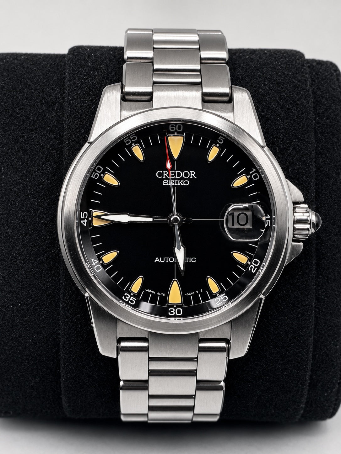 A Seiko Credor Automatic watch with a black dial, silver stainless steel case and bracelet, and yellow-gold hour markers, displayed on a black velvet watch roll.