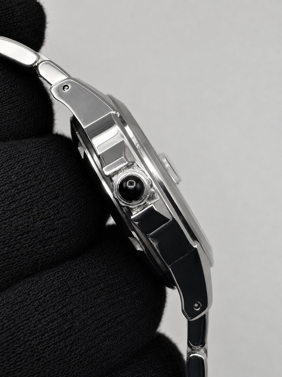 Close-up side profile of a silver-toned metal watch held against a black textured fabric background, showing the side case detail and crown.