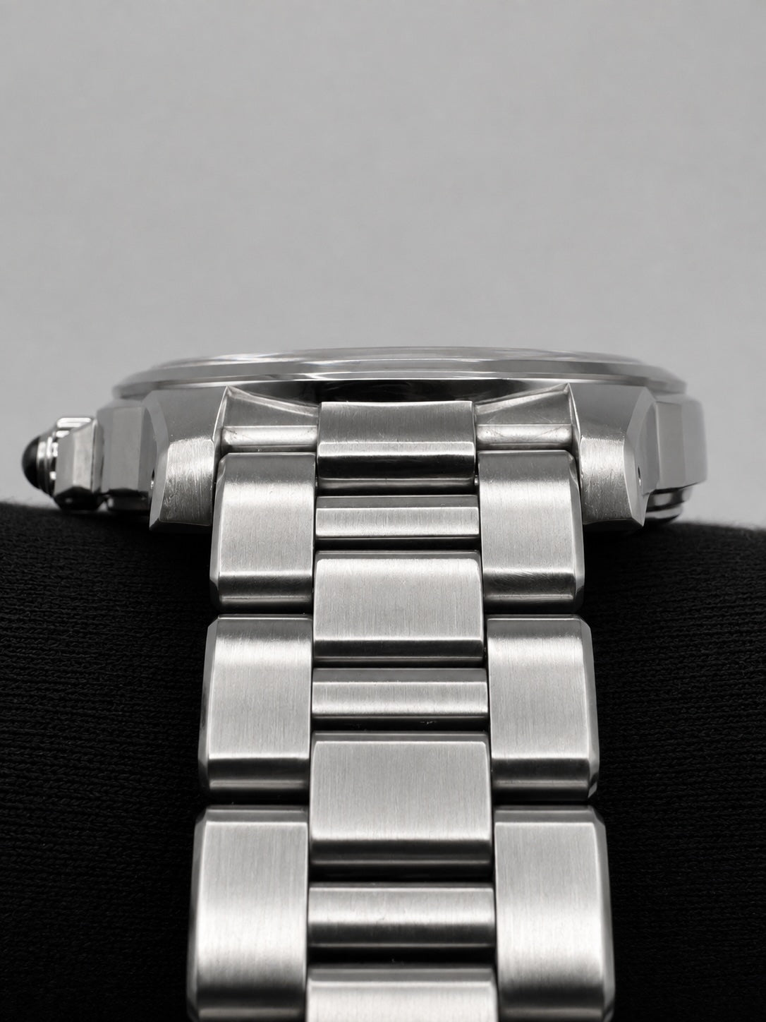Close-up of a stainless steel watch bracelet with a brushed metal finish, resting on a black textured surface against a light gray background.