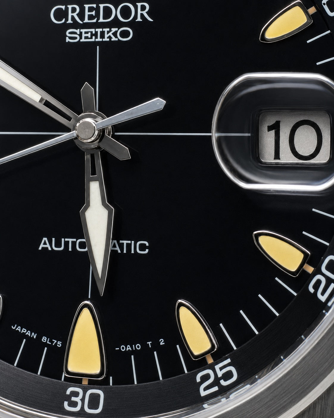 Close-up of a black Credor Seiko automatic watch dial with silver hands, yellow-gold hour markers, and a date window showing 10.