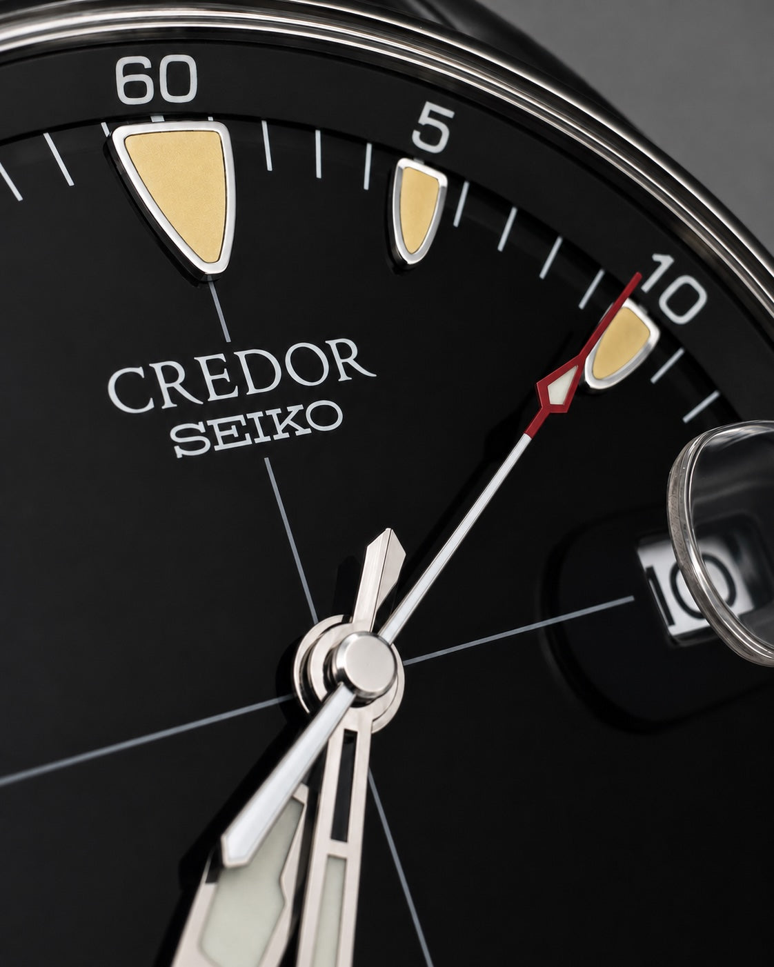 Close-up of a Credor Seiko watch dial with a black face, silver hands and markers, gold hour markers, and a red seconds hand.