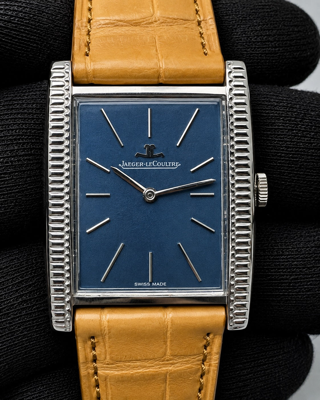 A vintage Jager-Le Coultre watch with a blue dial, silver-tone rectangular case with fluted sides, and a tan leather strap, shown resting on a black textured surface.