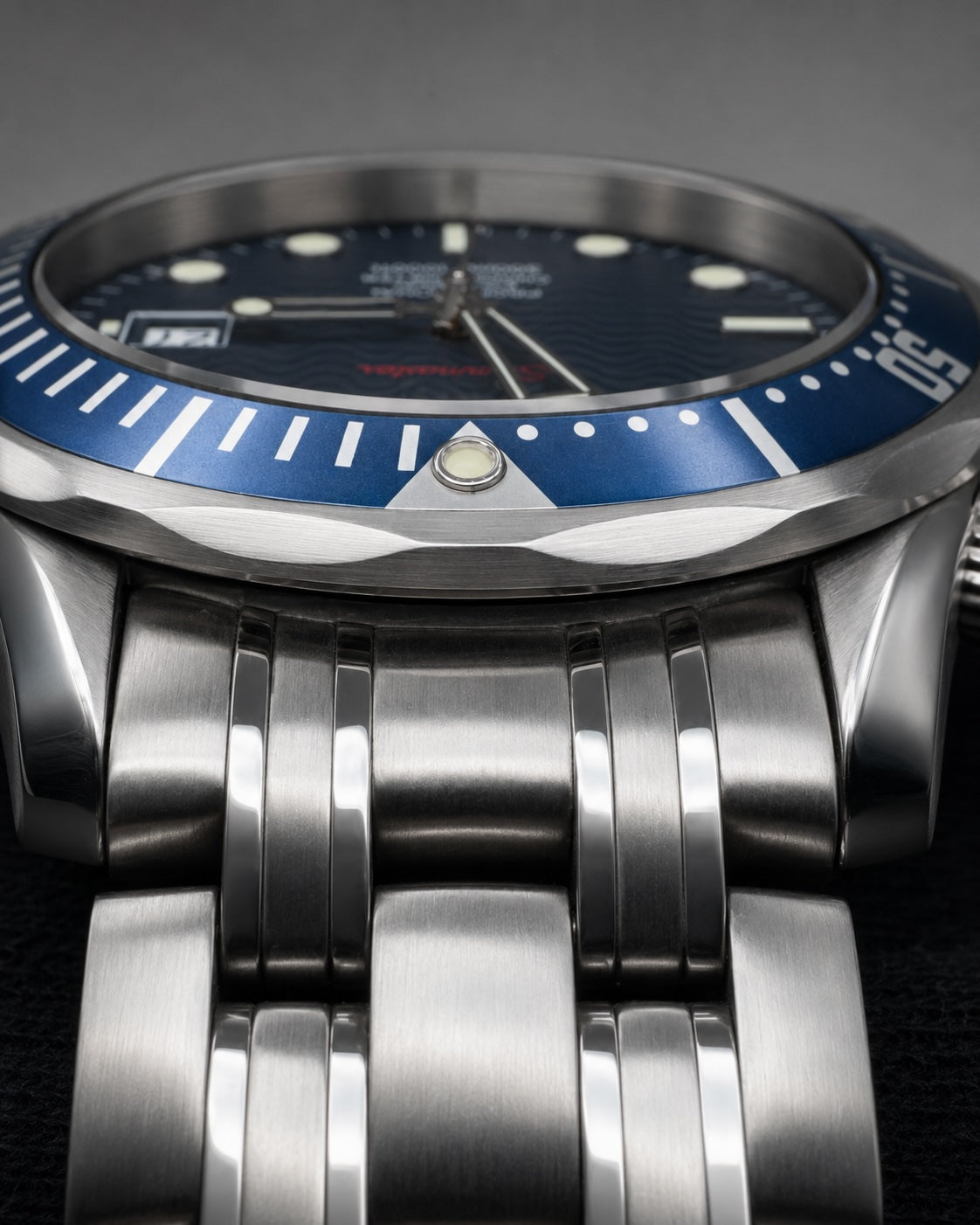 Close-up of a stainless steel wristwatch with a blue dial and blue rotating bezel, paired with a matching steel link bracelet.