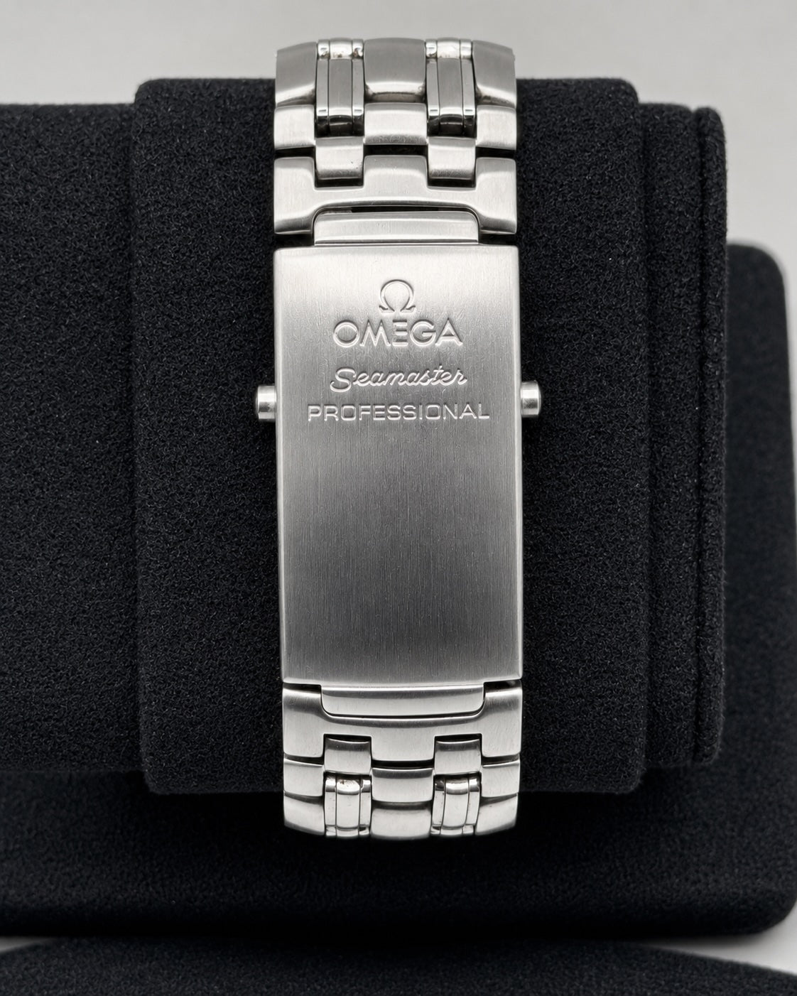 Close-up of an Omega Seamaster Professional stainless steel watch band clasp, displayed on a black velvet watch cushion.