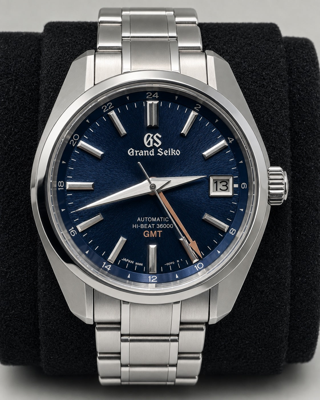 A Grand Seiko stainless steel wristwatch with a deep blue dial, silver-tone case and bracelet, and a date window, displayed on a black velvet watch stand.