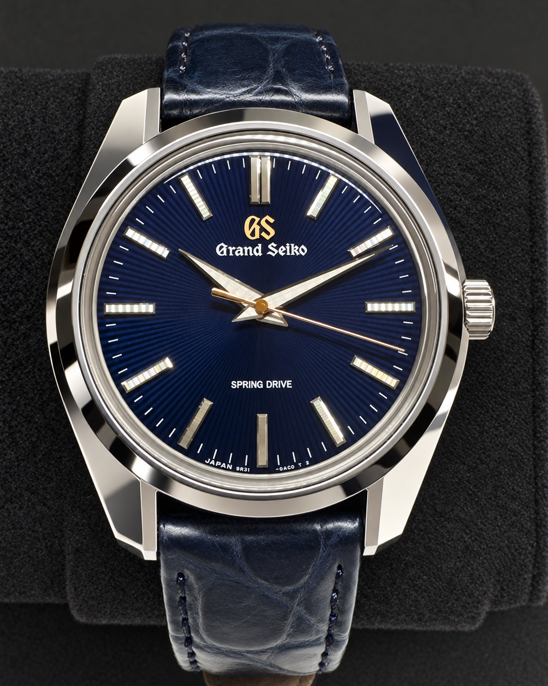 A Grand Seiko Spring Drive watch with a deep blue sunburst dial, silver-toned stainless steel case, and a matching dark blue leather strap, displayed on a black textured cushion.