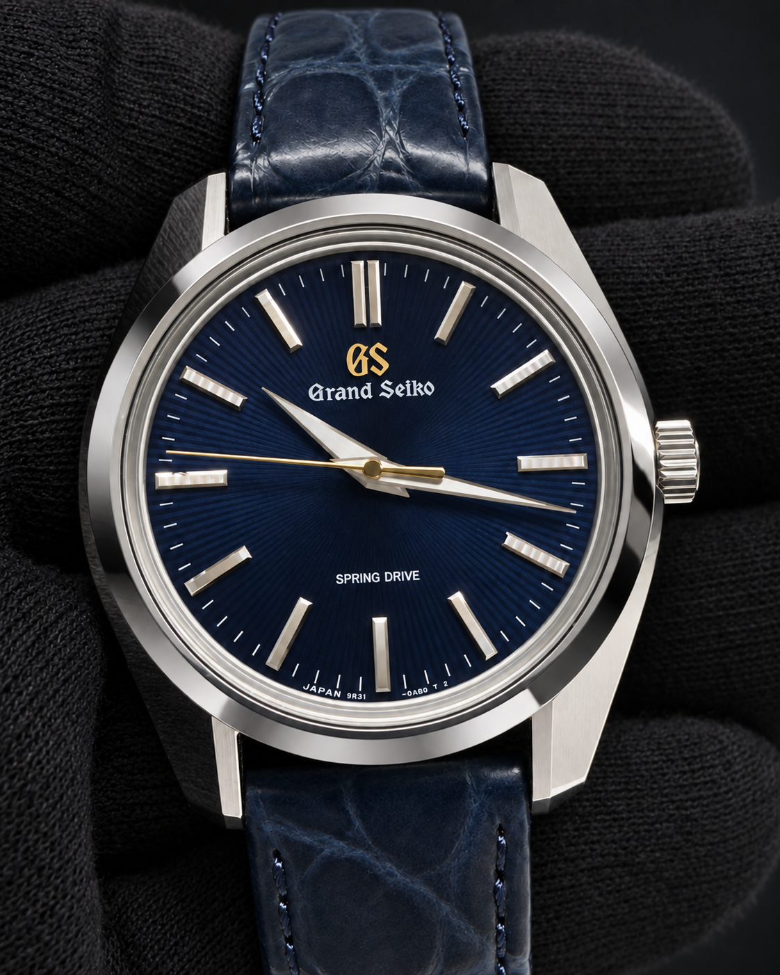 A Grand Seiko wristwatch with a deep blue sunburst dial, silver-toned stainless steel case, and a matching dark blue leather strap, presented on a textured black fabric background.