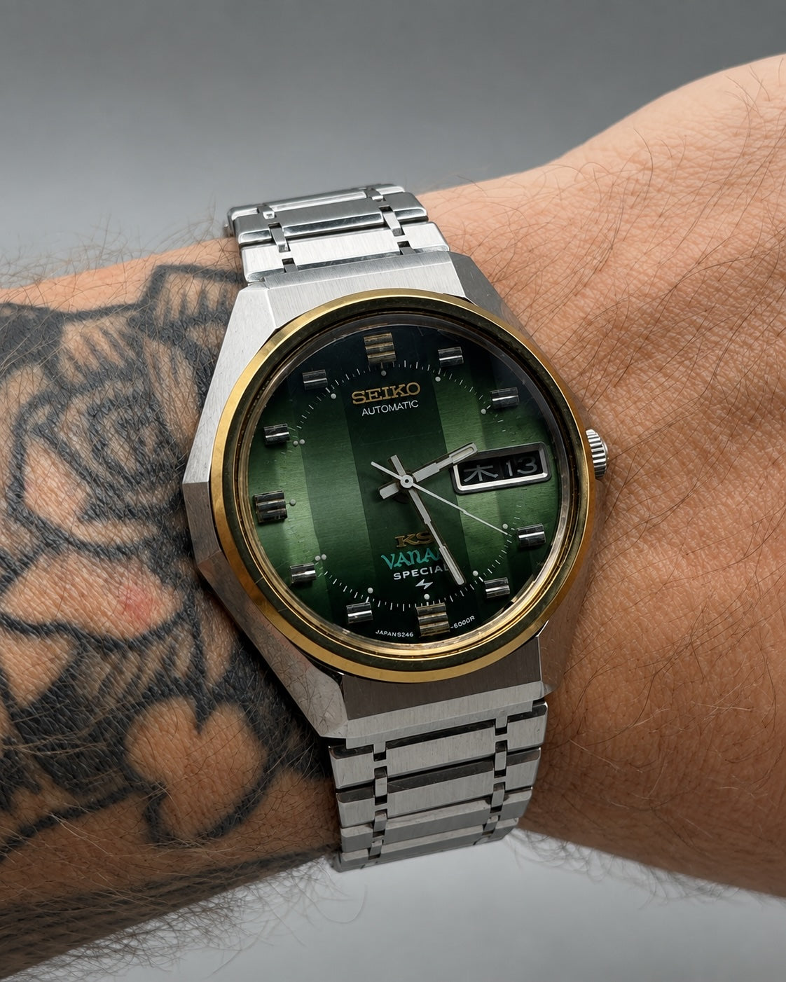 A wrist wearing a Seiko Vautier automatic watch with a green dial, silver-toned metal case and bracelet, and a gold-tone bezel, shown against a neutral gray background.
