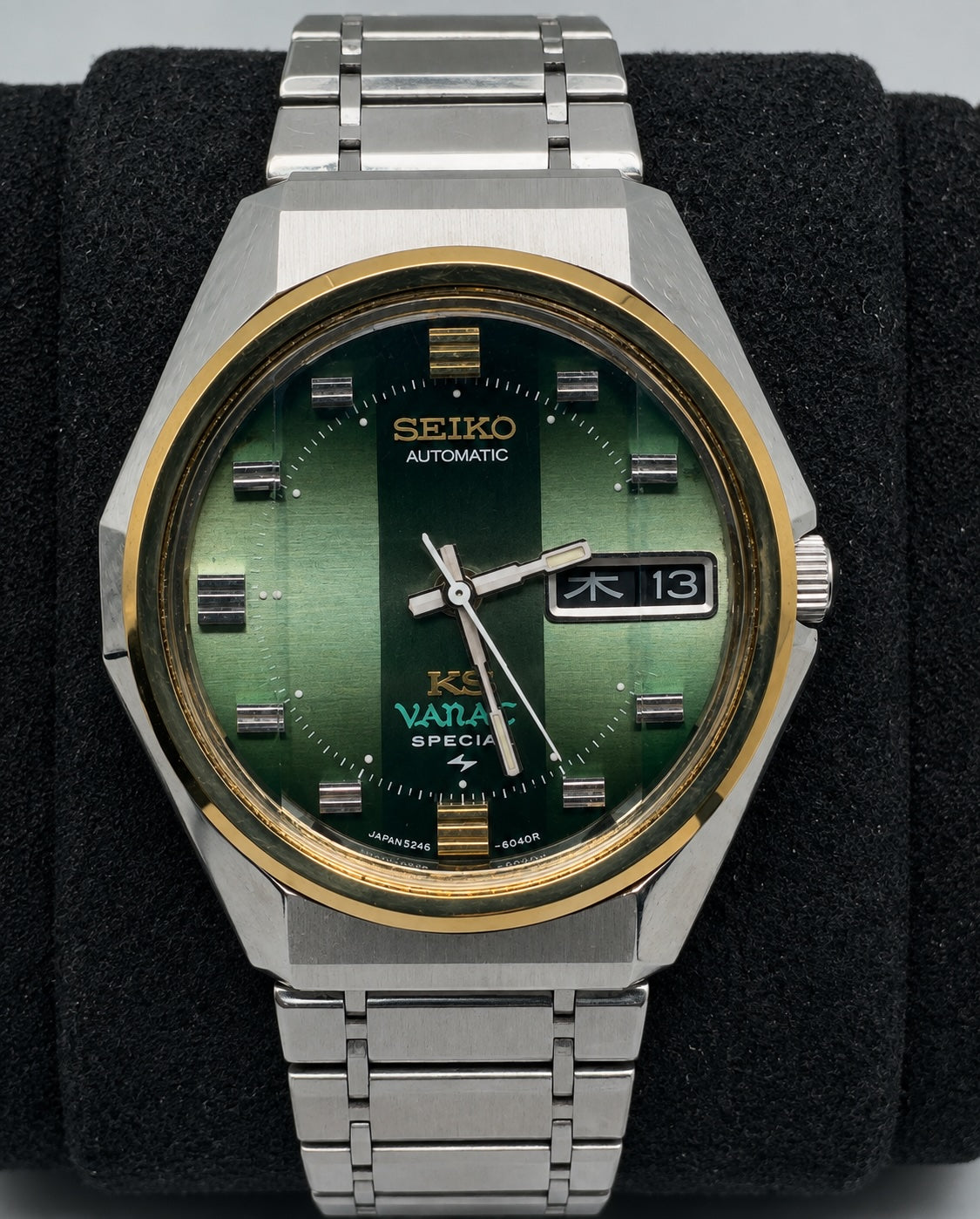 A vintage Seiko automatic watch with a green dial, silver-tone stainless steel case and bracelet, and a gold-tone bezel, displayed on a black felt watch cushion.
