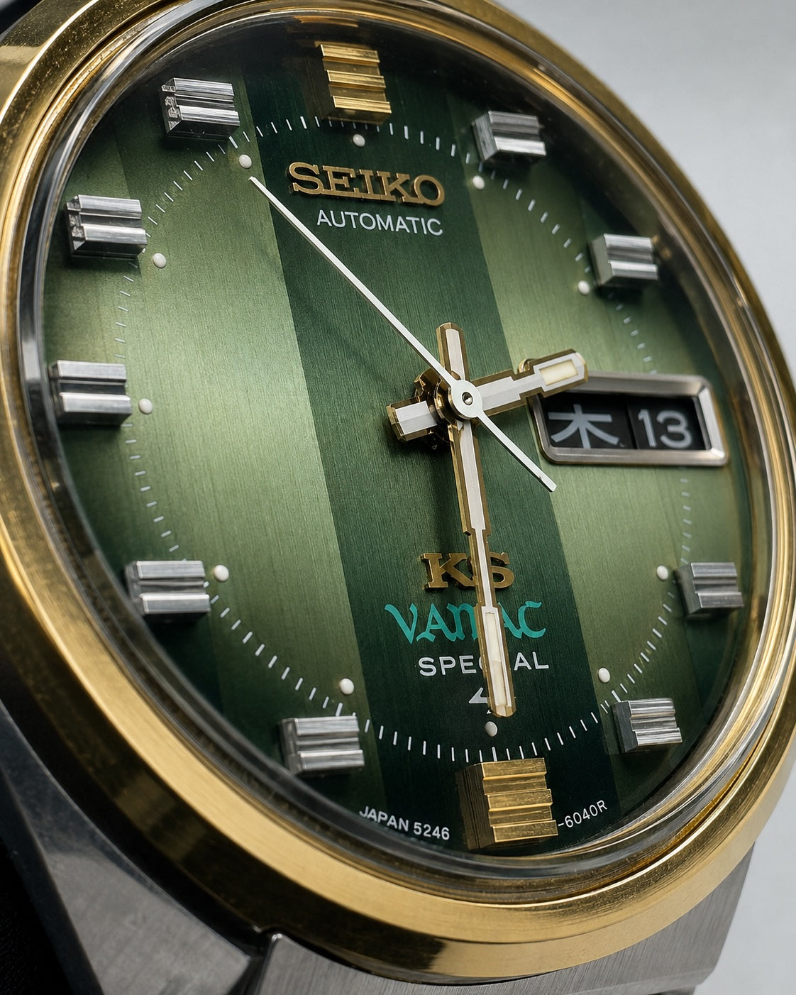 Close-up of a Seiko automatic watch dial with a green striped design, gold-tone bezel and hands, silver rectangular hour markers, and a date window.