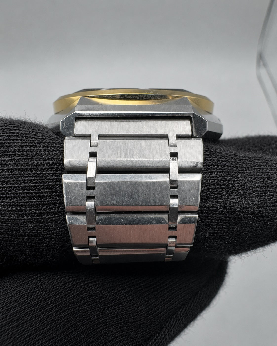 Close-up of a stainless steel link bracelet watch band with a brushed finish, resting on a black textured surface against a light gray background.